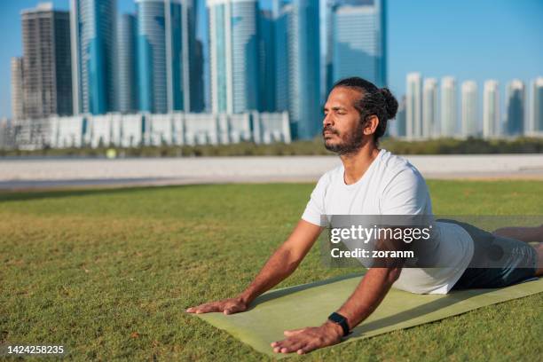 homme pratiquant le yoga sur la pelouse dans un parc public à abu dhabi, allongé sur le devant dans la pose cobra - arabie photos et images de collection