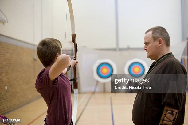 archery coach teaching a young archer to shoot. - bow arrow stock-fotos und bilder