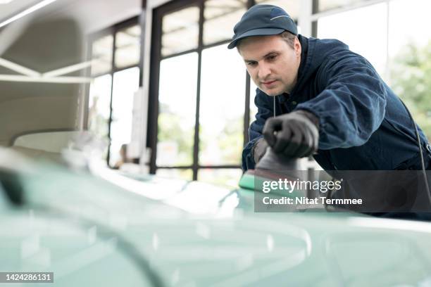 mechanic working in garage shop on classic car while using a portable handheld polisher to polish on car hood outer. classic car servicing, repair, and restorations - classic car restoration stockfoto's en -beelden