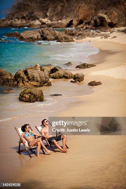 young coupld relaxing in charis on rocky beach - puerto vallarta stockfoto's en -beelden