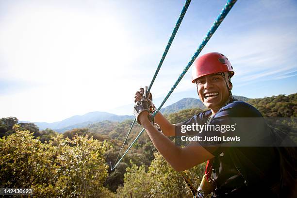 guy smiling with hands on zip line over tree tops - zipline stock pictures, royalty-free photos & images