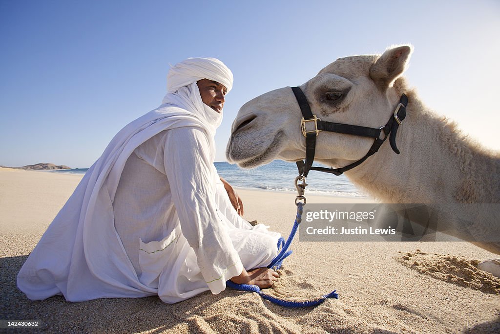 Camel and guide sitting on sandy beach in sun