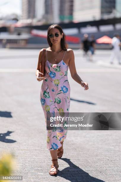 Guest is seen wearing Ray-Ban shades, gold pendant necklace, a light pink flower pattern satin long dress, brown leather shoulder bag and brown...