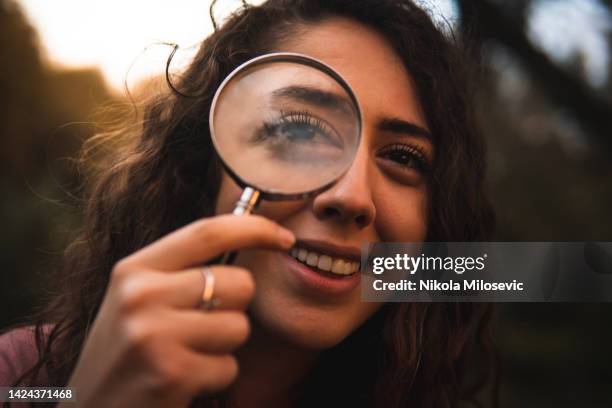 smiling caucasian girl holding a magnifying glass over her eye - lupe stock pictures, royalty-free photos & images