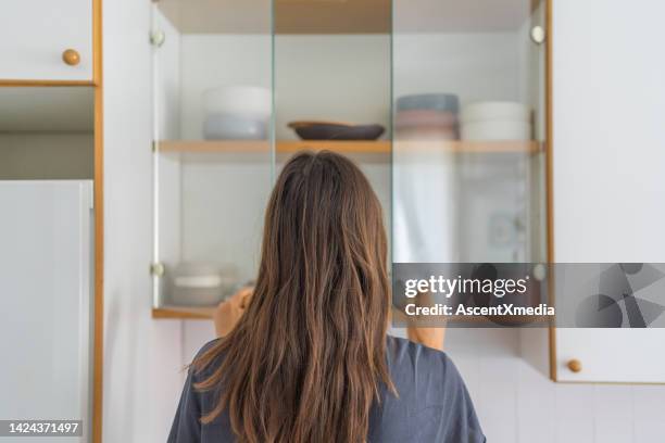 young woman opens cupboard for dishes - cabinet door stock pictures, royalty-free photos & images