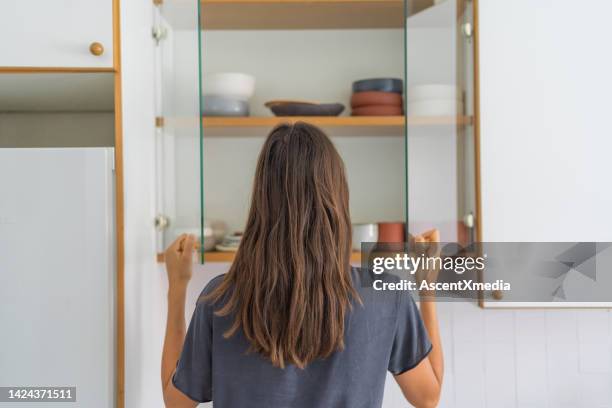 young woman opens cupboard for dishes - cabinet door stock pictures, royalty-free photos & images