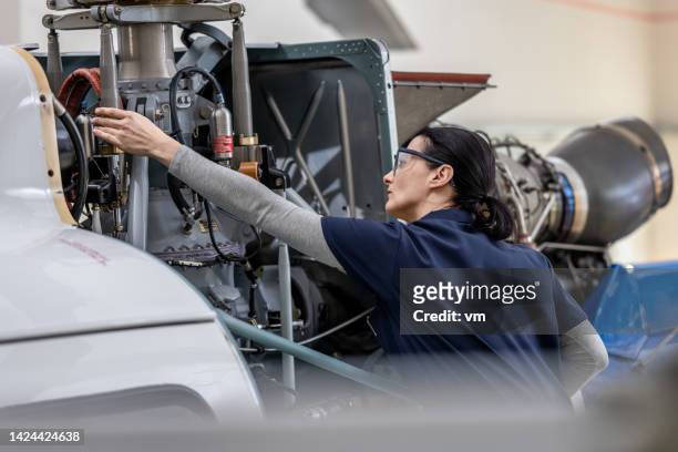 Aero engineer wearing protective glasses examining helicopter in hangar, mid shot