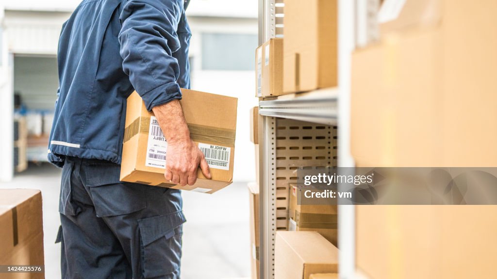 Warehouse worker holding cardboard box, unloading truck