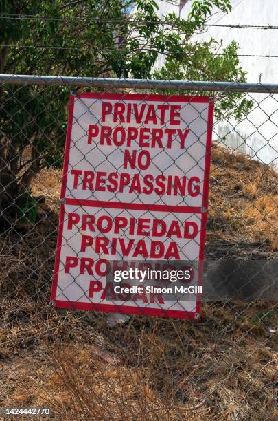 bilingual english- and spanish-language 'private property, no trespassing/propiedad privada, prohibido pasar' sign on a chain-link fence around a vacant lot - no trespassing segnale inglese foto e immagini stock