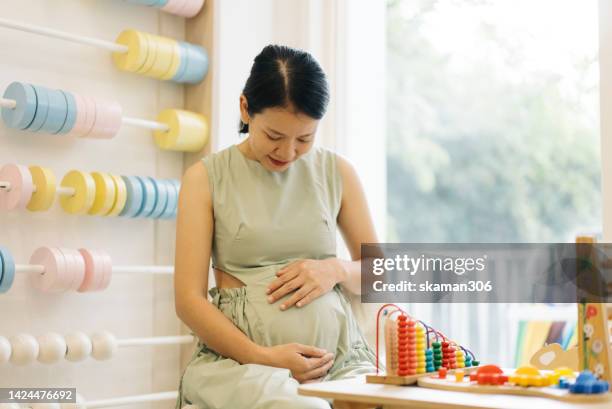 facial expression asian young adult mother very delighted to pregnant and touching tummy - medium shot stock pictures, royalty-free photos & images