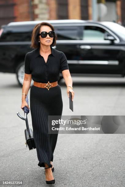 Guest wears black sunglasses, a black ribbed / short sleeves / midi dress, a camel shiny leather large belt, a black shiny leather handbag, a black...