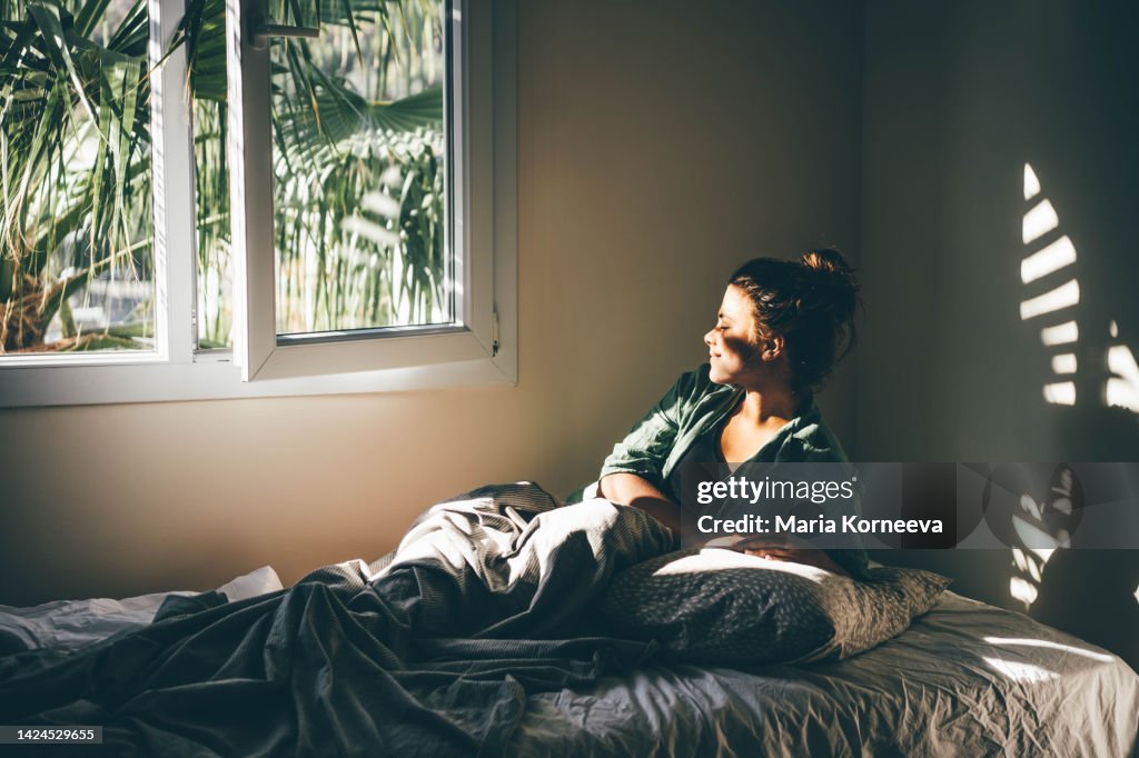 Woman waking up and relaxing near window at home.