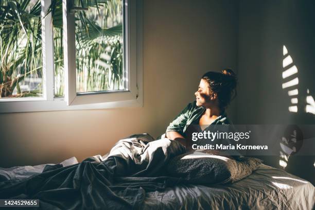 woman waking up and relaxing near window at home. - despertar fotografías e imágenes de stock