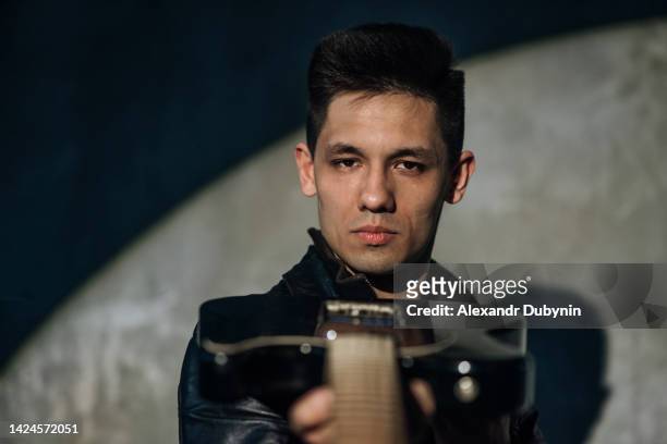 asian man with a musical instrument in his hands looking at the camera - electric guitarist stock pictures, royalty-free photos & images