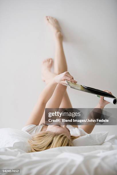 caucasian woman laying in bed reading magazine - reading magazine stock-fotos und bilder