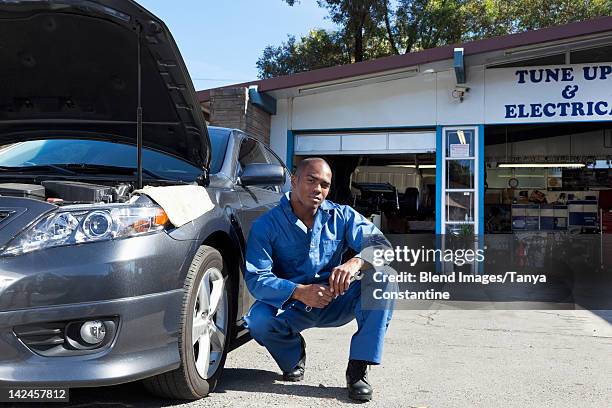 black mechanic squatting near car - macacão preto imagens e fotografias de stock