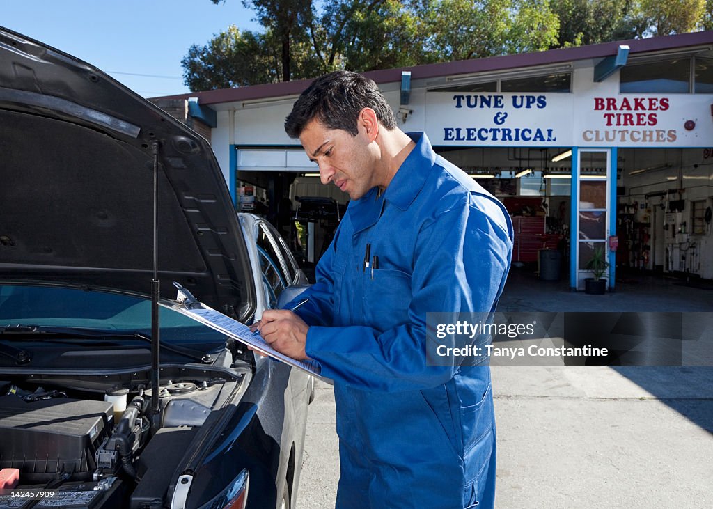 Middle Eastern mechanic writing on clipboard