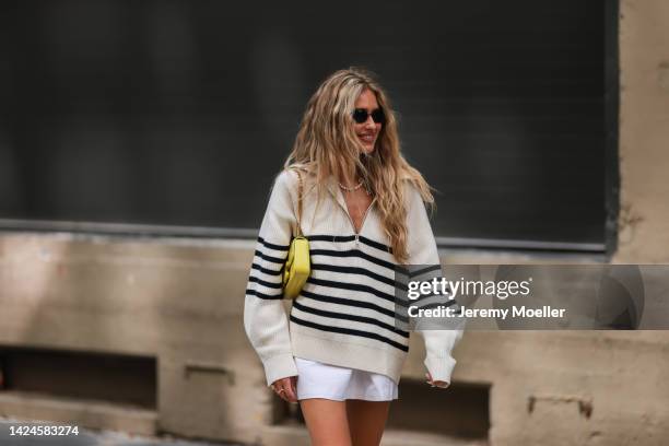 Emili Sindlev is seen wearing black sunglasses, pearl necklace, white striped wool knit sweater with a zipper, white short skirt and a yellow leather...