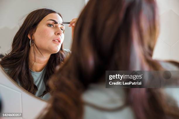 woman fixing make-up in front of the bathroom mirror - eyebrow pencil stockfoto's en -beelden