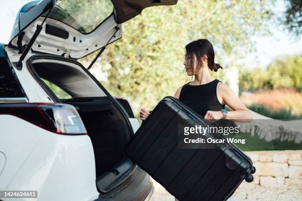 young woman loading luggage into car, getting ready for a road trip - auto mieten stock-fotos und bilder