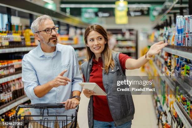 saleswoman assisting male shopper in supermarket - supermarket staff stock pictures, royalty-free photos & images