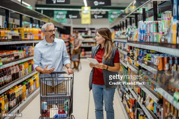 verkäuferin, die reifen männlichen käufer im lebensmittelgeschäft unterstützt - supermarket help stock-fotos und bilder