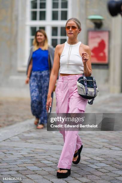 Guest wears orange sunglasses, gold and diamonds earrings, a brown suede necklace, a white ribbed halter-neck / cropped tank-top, pale pink large...