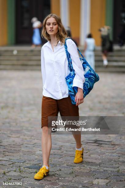 Guest wears a white shirt, brown long shorts, a blue print pattern oversized shoulder bag, white socks, yellow shiny leather with black logo pattern...