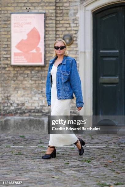 Guest wears black sunglasses, a blue denim jacket, a white latte ribbed tank-top / cut-out waist long dress, black shiny leather block heels...