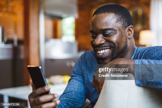 fröhlicher mann, der videokonferenzen mit einem freund genießt, während er zu hause faulenzt - afro amerikanische kultur stock-fotos und bilder