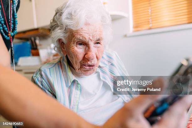 une femme âgée âgée de race blanche qui regarde de près un membre de sa famille ou un soignant lui montre une vidéo amusante ou une publication sur les médias sociaux sur un téléphone intelligent - centenaire et plus photos et images de collection