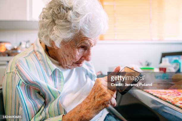 elderly senior caucasian woman looking closely and using her index finger to digitally e-sign the touch screen on a smart phone mobile device - looking closely stock pictures, royalty-free photos & images