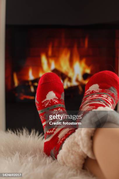 warming her feet by the fireplace while wearing cozy christmas themed socks - socks fireplace stock pictures, royalty-free photos & images