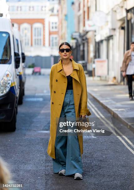 Julia Haghjoo wears mustard yellow double breasted coat, blue pants, brown bag, black top outside Eudon Choi during London Fashion Week September...