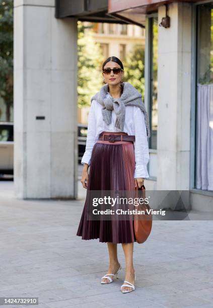 Julia Haghjoo wears pleated high waisted skirt, brown bag, white button shirt, sandals, grey jumper around shoulders, sunglasses outside Huishan...