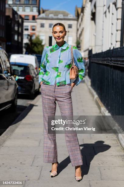 Alina Baikova wears checkered pants, blue green blouse with print, Chanel bag outside Paul & Joe during London Fashion Week September 2022 on...
