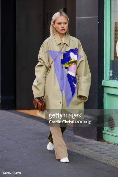 Guest wears beige coat with print, brown bag, two tone pants, white shoes outside Eudon Choi during London Fashion Week September 2022 on September...