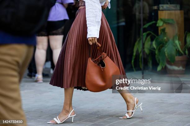 Julia Haghjoo wears pleated high waisted skirt, brown bag, white button shirt, sandals, grey jumper around shoulders, sunglasses outside Huishan...