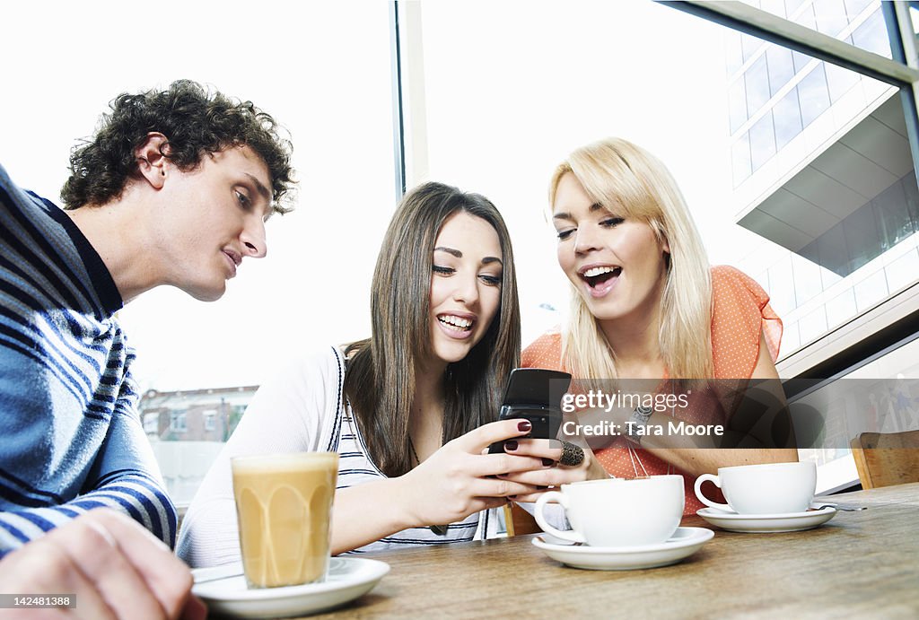 Three young adults in cafe looking at mobile phone