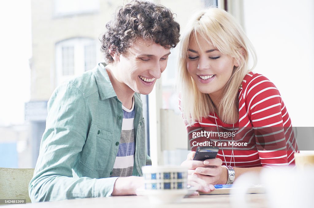 Young man and woman looking at phone on cafe