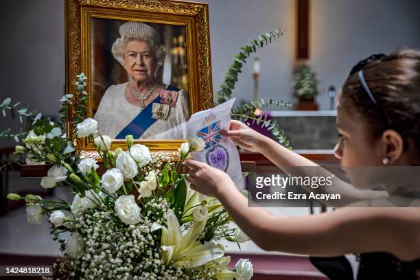 Girl places a drawing next to a portrait of the late Queen Elizabeth II following a memorial service at the Holy Trinity Anglican Episcopal Church on...