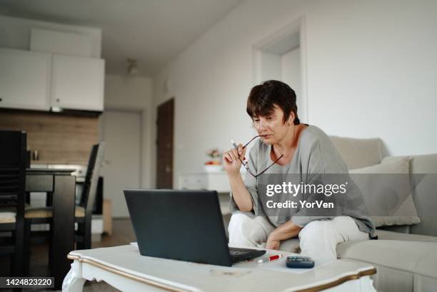 mature woman wearing glasses calculating domestic expenses and paying bills with e-banking application during economic inflation - house rental stock pictures, royalty-free photos & images
