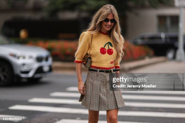 Emili Sindlev seen wearing statement wool sweater with cherries and plaid skirt, outside coach during new york fashion week on September 12, 2022 in...