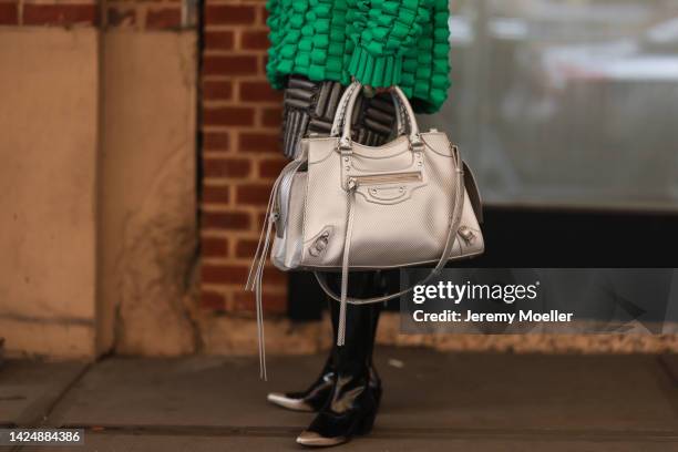 Val is seen wearing green oversize knit sweater, grey pattern shorts, black shiny leather high boots and a silver leather Balenciaga bag, outside...