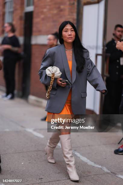 Guest is seen wearing an orange short dress, grey blazer jacket, beige Bottega Veneta Chain Pouch bag and beige high boots, outside Jonathan Simkhai,...