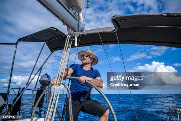 un homme portant un chapeau de paille conduit un voilier et en profite. - sailing greece photos et images de collection