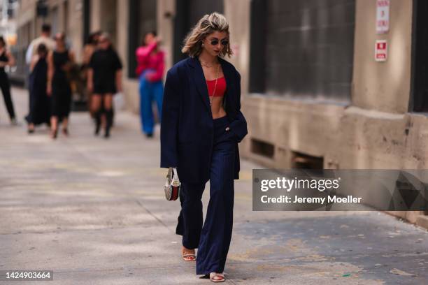 Guest is seen wearing black sunglasses, gold large earrings, gold long chain necklace, red cropped top, a navy blue striped print pattern oversized...