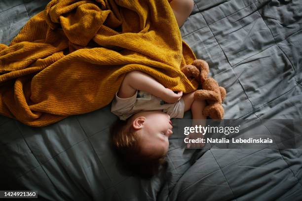 baby toddler sleeps covering yellow plaid on bed, authentic home photo. - sleeping toddler bed fotografías e imágenes de stock