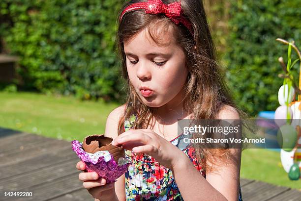 girl eating chocolate easter egg in garden - chocolate foil stock pictures, royalty-free photos & images