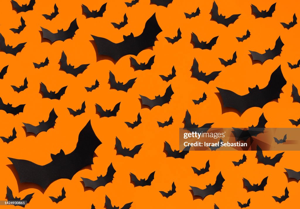 Image of a large group of handmade black bats made of paper on a plain orange background. Halloween concept.